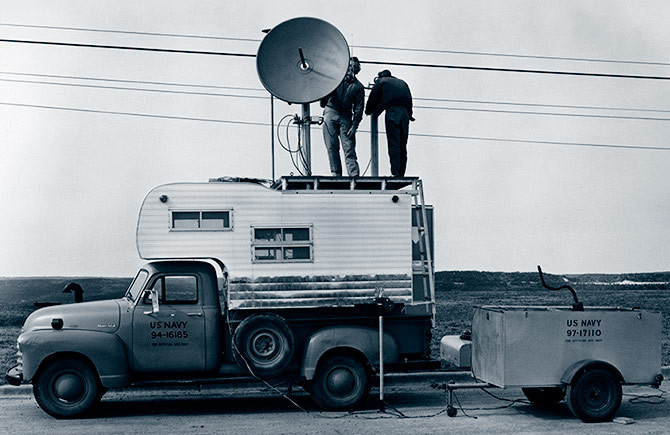 Two men with transmitters on top of a truck with a camper in the bed using radio transmitters in the late 1940s-1950s