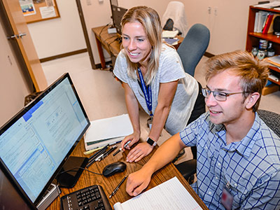 research scientist standing with student working on computer